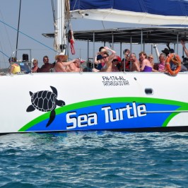 Catamaran named Sea Turtle with people on deck, sailing in clear blue water.