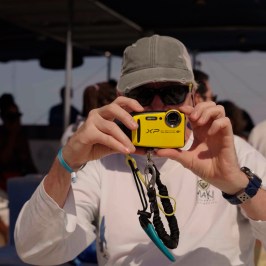 Person in a hat taking a photo with a yellow camera on a boat.