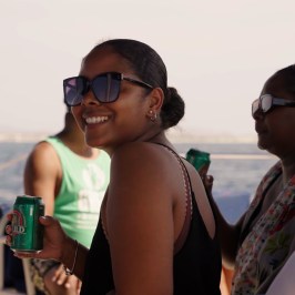 People smiling and holding drinks on a boat with water in the background.