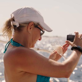 Woman on a boat takes a photo with a camera while holding a drink.