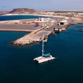 Aerial view of a marina with docked boats and a catamaran sailing nearby.