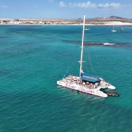 Catamaran with people in turquoise sea near a coastline with buildings.