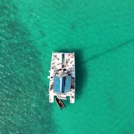Top view of a catamaran with people on turquoise water.